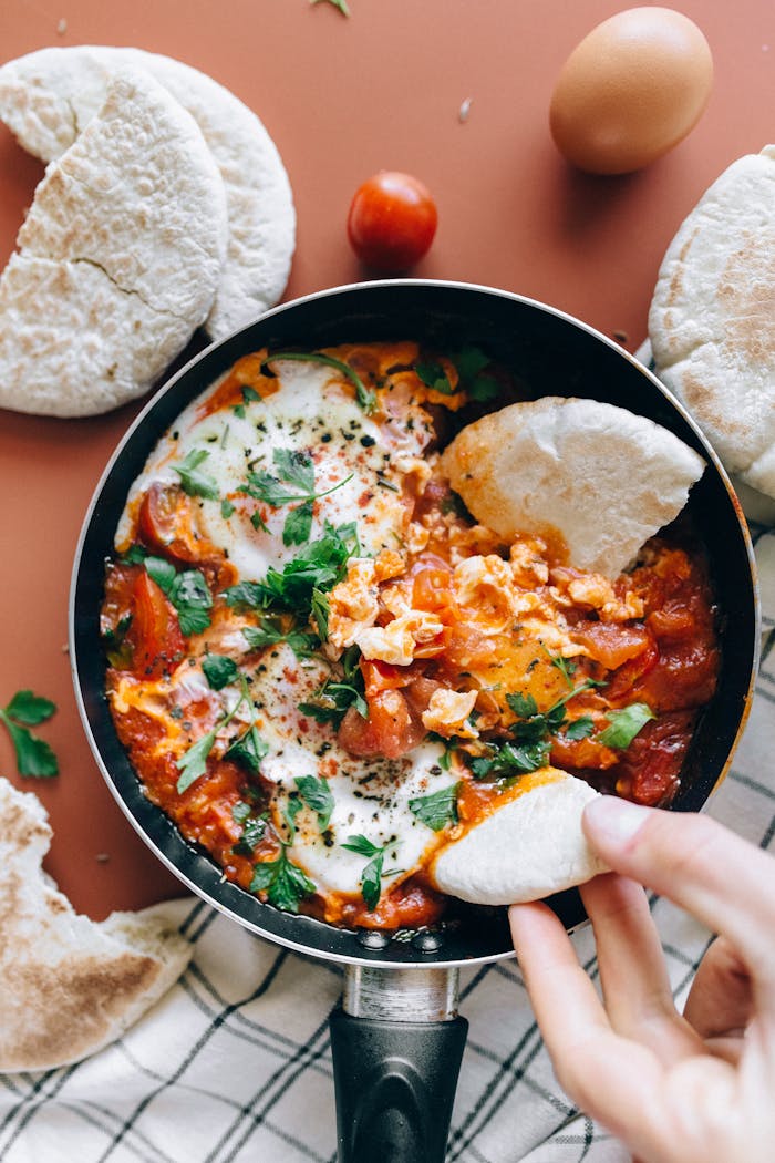 Über Uns Savor a classic Shakshuka dish with vibrant tomatoes, eggs, and herbs served with fresh pita bread.